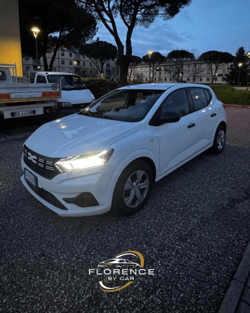 White Dacia rental car by Florence by Car parked outdoors at dusk, with buildings and pine trees in the background.